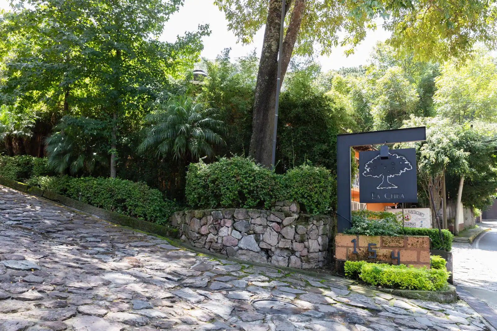 La entrada del Residencial La Ceiba, con su letrero entre jardines y el camino empedrado